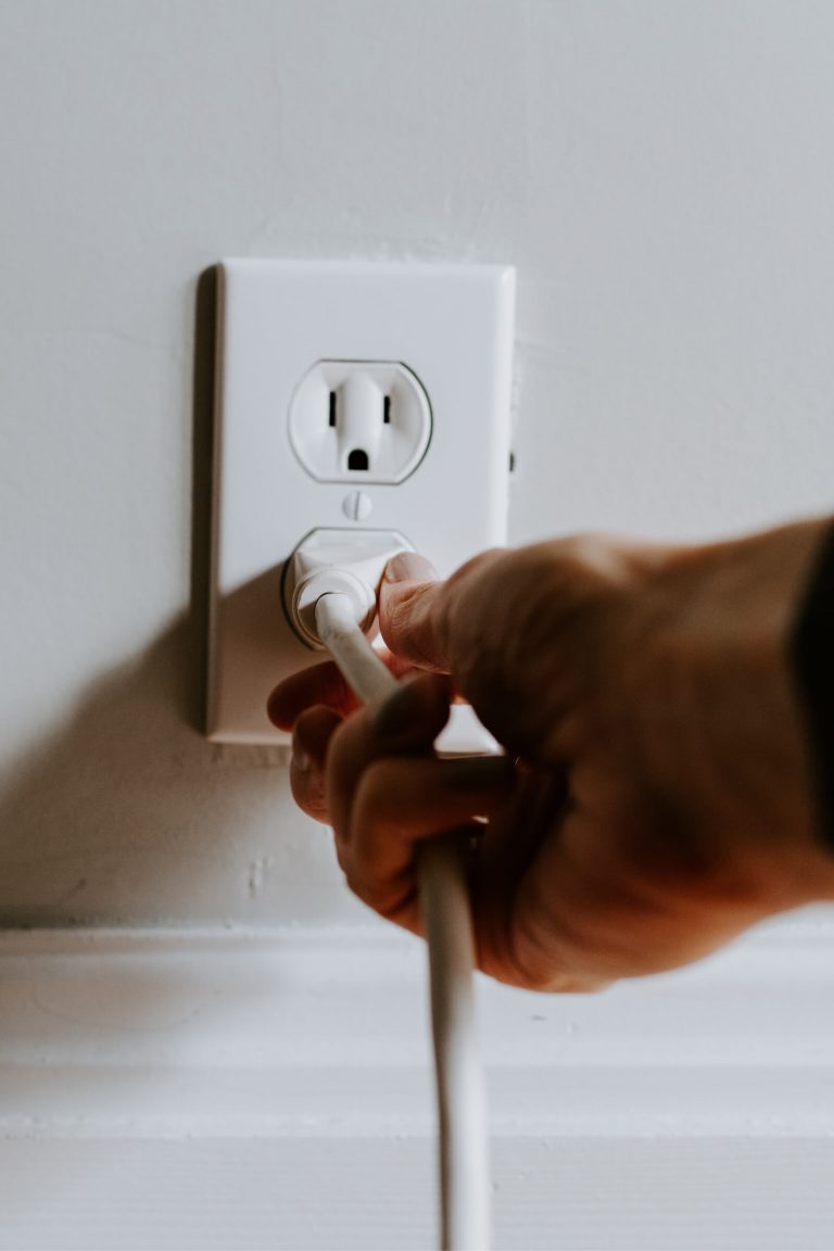 A man’s hand and wrist inserting a plug into a plug socket in a wall